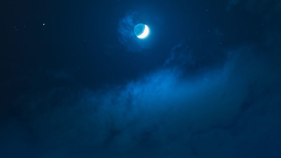 A beach with waves of water at night under the light of a crescent moon