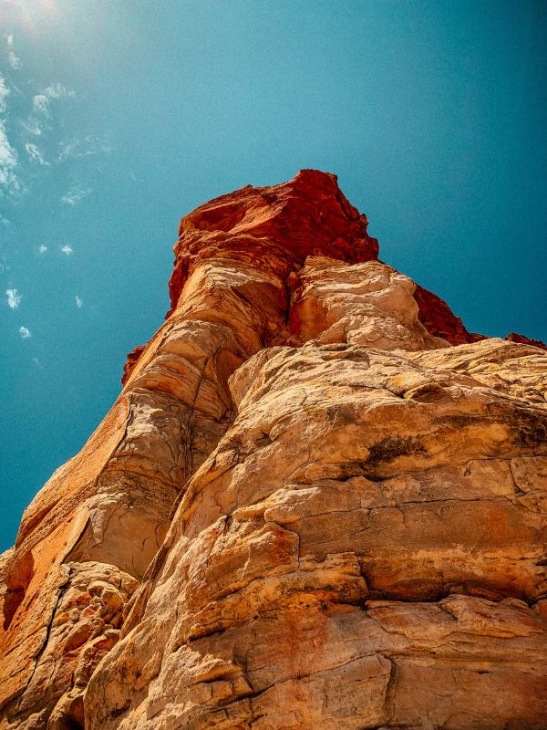 View from below of a reddish-brown rocky cliff with a blue-green sky background